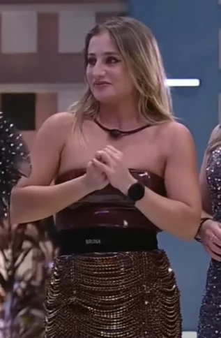 Bruna Griphao standing indoors at an event, hands clasped, wearing a strapless outfit.