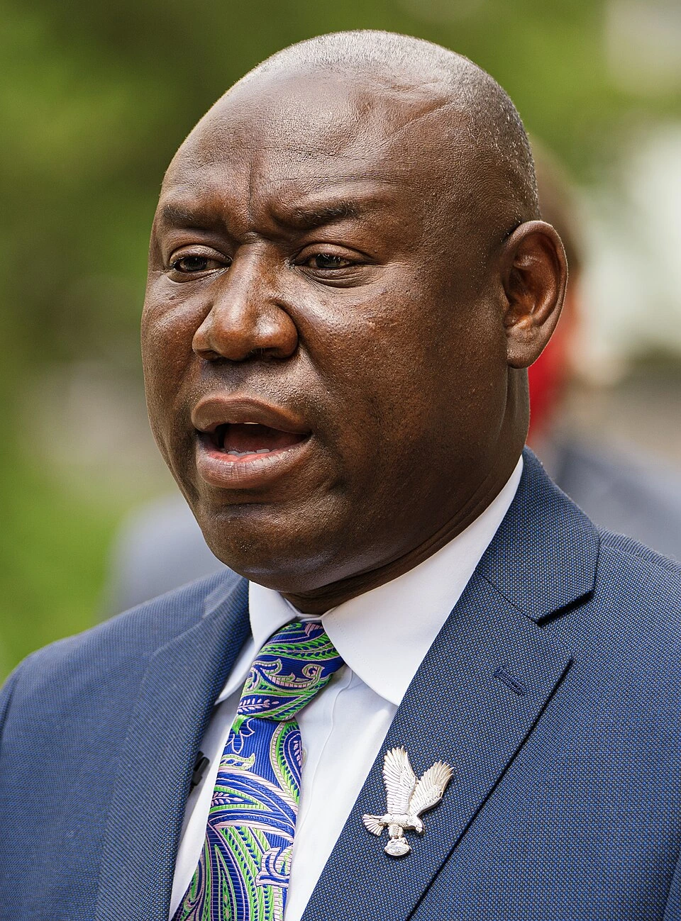 Ben Crump speaking outdoors in a blue suit and patterned tie